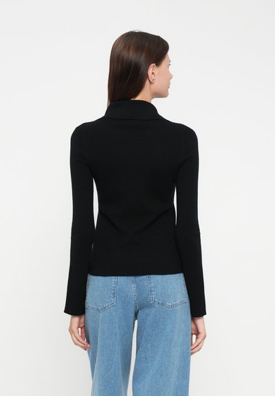 Svart strikkegenser med høy krage, tettsittende silhuett og lange ermer, kombinert med lyseblå vide jeans.