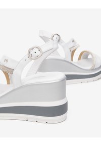 Sandalias de cuña blancas de cuero con correas para el tobillo ajustables, que cuentan con un acento brillante y una suela gruesa en tonos gris y blanco.