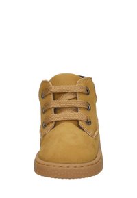 Tan suède enkellaars met een ronde neus, rubberen zool, zes oogjes en gestructureerde veters. Stikselaccent langs de kraag.