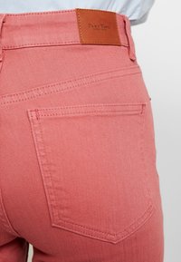 Acercamiento del bolsillo trasero de unos vaqueros de mezclilla rosa con costuras visibles y una etiqueta de cuero marrón etiquetada "Part Two Copenhagen".