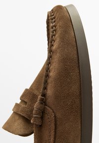 Brun mockaloafer med dekorativa sömmar, tofsdetalj på vristen och mörk gummisula.