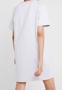 Person som bär en ljusgrå kortärmad avslappnad klänning, visad bakifrån med armarna avslappnat vid sidorna.