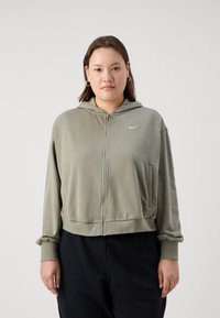 Sudadera con cremallera en verde oliva, con capucha, bolsillos frontales y puños de canalé. Presenta un pequeño logo blanco en el pecho y una textura suave.