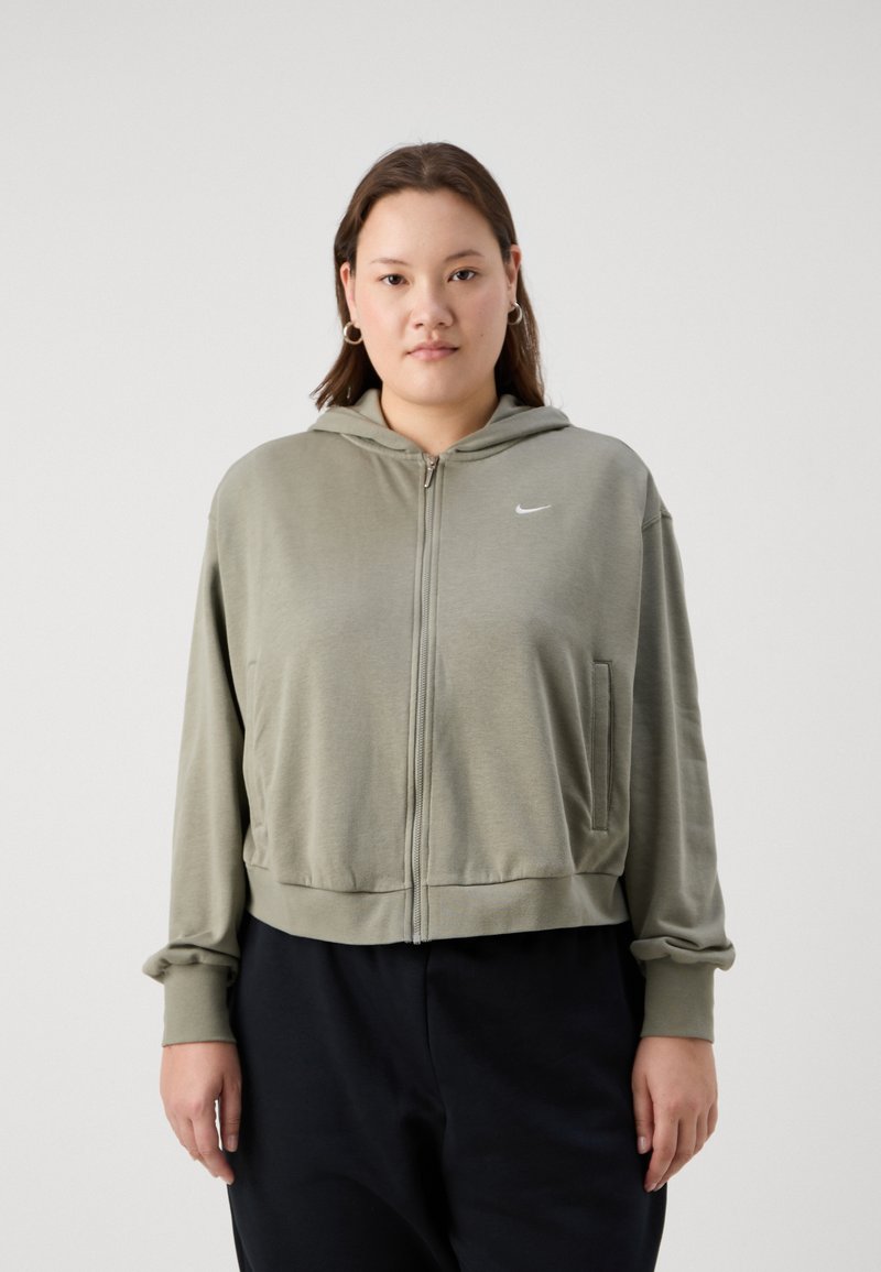Sudadera con cremallera en verde oliva, con capucha, bolsillos frontales y puños de canalé. Presenta un pequeño logo blanco en el pecho y una textura suave.