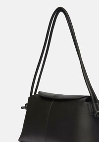 Czarna skórzana torebka o wyrazistym kształcie, z klapą na skład, dwiema smukłymi paskami oraz gładką teksturą. Detale minimalistycznego wzornictwa.
