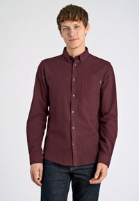 Bordeaux knoopshirt in een textuurstof met een borstzak, met knopen en een gestructureerde kraag. Gecombineerd met donkere jeans.
