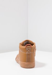 Bota de tobillo de cuero marrón con costuras blancas, punta redonda y suela de goma. Presenta un lazo de etiqueta de tela en la parte posterior y un logo grabado en el tacón.