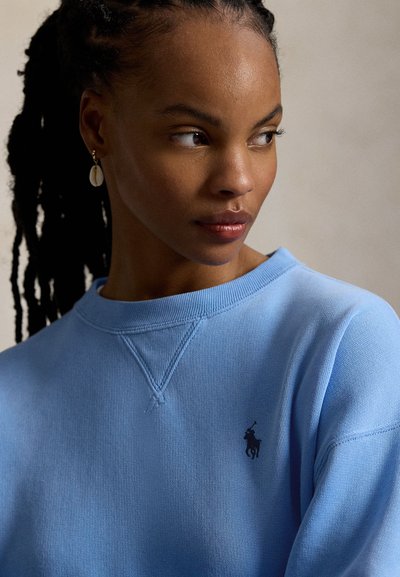 Φωτεινή γαλάζια φούτερ από βαμβάκι με ριμπ μανσέτες και λαιμόκοψη. Διαθέτει μικρό μαύρο λογότυπο στο στήθος. Λεία υφή.