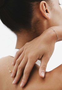 Pulsera de plata con pequeños acentos redondos, llevada en una mano que descansa sobre el cuello. La piel tiene un tono cálido y una textura suave, el fondo es claro.