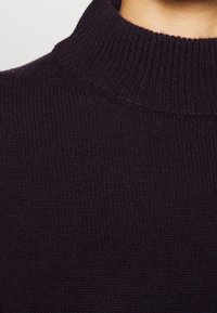 Detailní záběr na černý žebrovaný rolák, který ukazuje texturovaný pletený vzor, vysoký límec a hladký povrch.