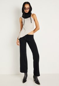 Top bege assimétrico com cachecol de malha preto anexado; combinado com calças pretas largas e botins pretos de bico.