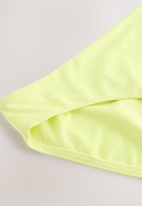 Lysegult stof med en glat tekstur, der viser en foldet kant og syningsdetaljer. Materialet virker let og elastisk.