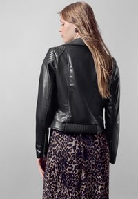 Giubbotto da motociclista in pelle nera con spalle rigate, polsi con zip e orlo aderente, abbinato a una gonna con stampa leopardata.
