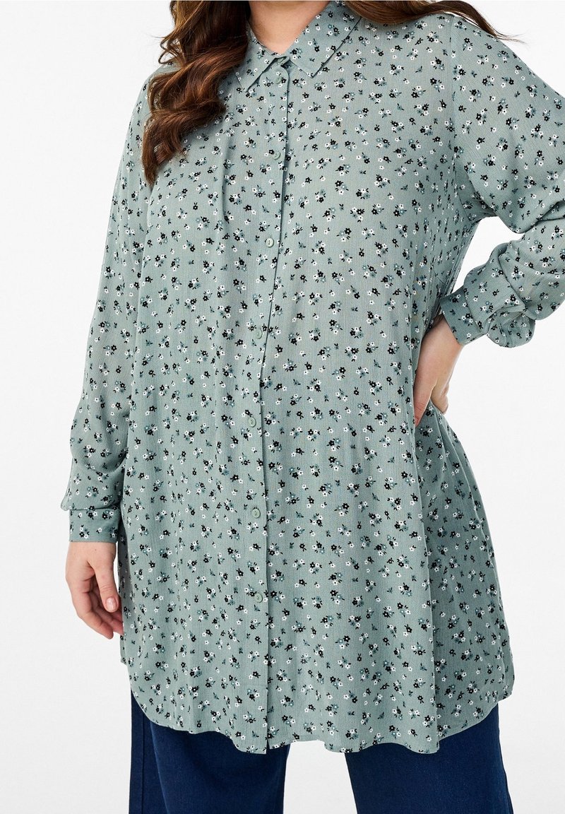 Camicia a maniche lunghe con bottoni in tessuto verde chiaro, decorata con piccoli motivi floreali bianchi e neri. Caratterizzata da un colletto classico e una vestibilità comoda.