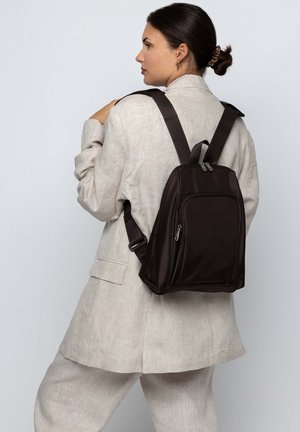 Brown, textured backpack with adjustable straps, featuring two zippered compartments and a sleek design. Worn over the shoulder.