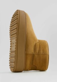 Tan suede ankle boot with a textured rubber sole, rounded shape, and visible stitching details. Features a low-profile design.