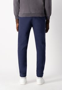 Navy blue sweatpants with a tapered design, made of soft fabric. Worn with white sneakers, showcasing a clean and simple look.