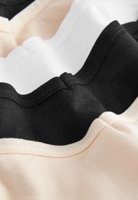 Zbliżenie na złożoną tkaninę pokazującą czarną, białą i beżową bawełnę z widocznym przeszyciem i teksturowanym wzorem dzianiny.