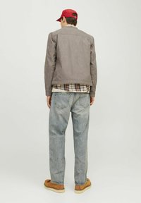 Jachetă din suede gri, cămașă în carouri dedesubt, blugi lejeri de culoare albastră deschisă și pantofi maro, văzută din spate cu o căciulă roșie.