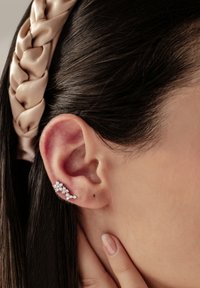 Orecchino in argento con più piccole gemme disposte in un design curvo, posizionato su un primo piano di un orecchio parzialmente visibile e capelli.