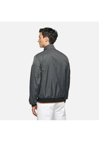 Giacca bomber grigia con colletto stondato, orlo e polsini elasticizzati, con dettagli arancioni. Tessuto liscio e materiale leggero.