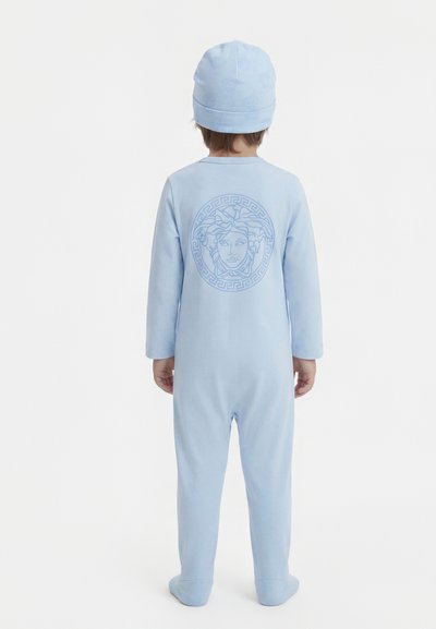 Παιδί που φοράει ανοιχτό μπλε φορμάκι με ποδολάστιχο και ταιριαστό καπέλο, με έμβλημα κεφαλής Μέδουσας στην πλάτη του φορμάκι, στέκεται γυρισμένο με την πλάτη.