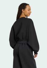 Sweatshirt noir à la coupe décontractée, avec des manches oversize, une taille côtelée et une texture douce, associé à un pantalon foncé assorti.