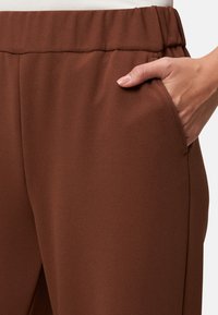 Pantalons marron avec taille élastique, en tissu lisse et texturé. Dotés d'une poche latérale et d'une coupe ajustée.