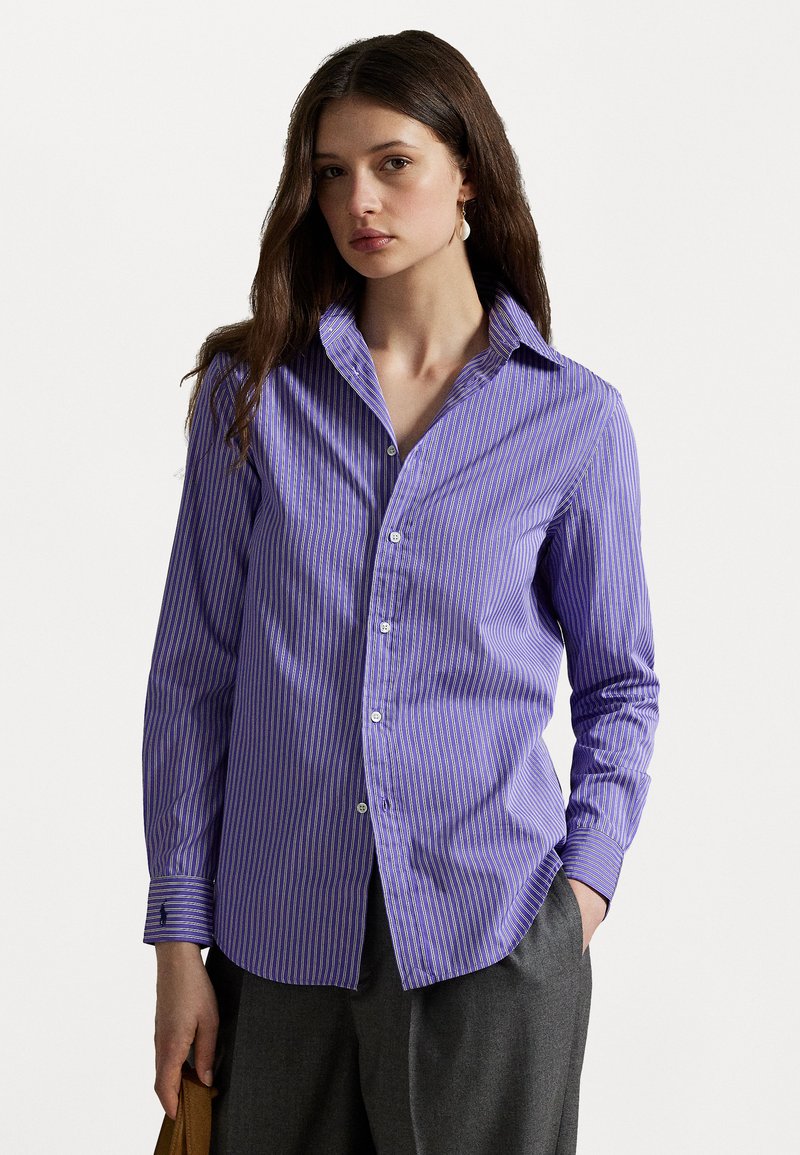 Chemise rayée violette à manches longues, avec un devant à boutons et un col classique. Présente une texture subtile et est associée à un pantalon gris.