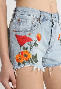 Světle modré džínové kraťasy s třepeným lemem a květinovou výšivkou v červené, oranžové a zelené barvě na přední straně pro zvýraznění detailů.
