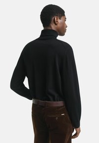 Mustat poolopaitaset näyttävät sileiltä pitkiltä hihoilta. Yhdistetty ruskeisiin corduroy-housuihin ja ruskeaan vyöhön, nähtynä takaa.