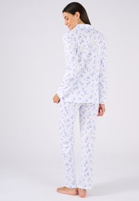 Ensemble de pyjama blanc avec un motif floral bleu, manches longues, col à boutons et pantalon à jambe droite. Tissu doux et léger.