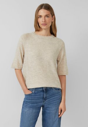 Pull en tricot beige à manches courtes et col rond, associé à un jean bleu. Texture douce, design décontracté, détails de couture visibles.