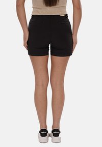 Pantaloni corti neri con finitura liscia, lunghezza fino a metà coscia e orlo piegato. Due tasche posteriori. Abbinati a scarpe da ginnastica bianche con logo nero.