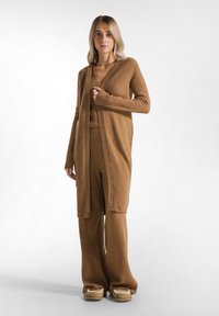 Lange cardigan met open voorkant en bijpassende broek van een zachte bruine stof. Heeft een v-hals ontwerp en een ontspannen pasvorm met lange mouwen en wijde pijpen.