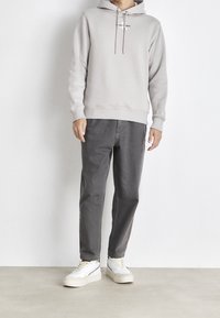 Světlý šedý mikina s kapucí a šňůrkami, doplněná o tmavě šedé kalhoty a bílé tenisky. Příjemný materiál, volný střih, minimalistický design.