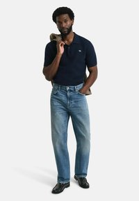 Mörkblå pikétröja med korta ärmar, kombinerad med ljusblå jeans och svarta skor. En rutmönstrad jacka hänger över axeln.