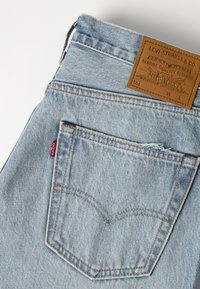 Πίσω τσέπη από ανοιχτό μπλε τζιν Levi's με καφέ δερμάτινη ετικέτα Levi Strauss & Co. και μικρή κόκκινη υφασμάτινη ετικέτα Levi's.
