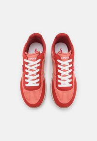 Baskets de sport rouges et roses avec une tige en daim et en mailles, lacets blancs et semelle texturée. Logo Levi's sur la languette.