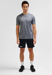 Gray short-sleeve athletic shirt with logo, paired with black shorts featuring a logo. Black shoes and white socks complete the look.