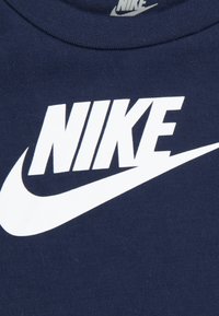 Tricou din bumbac albastru marin, cu un logo mare Nike alb și un design swoosh, material texturat și decolteu rotund.
