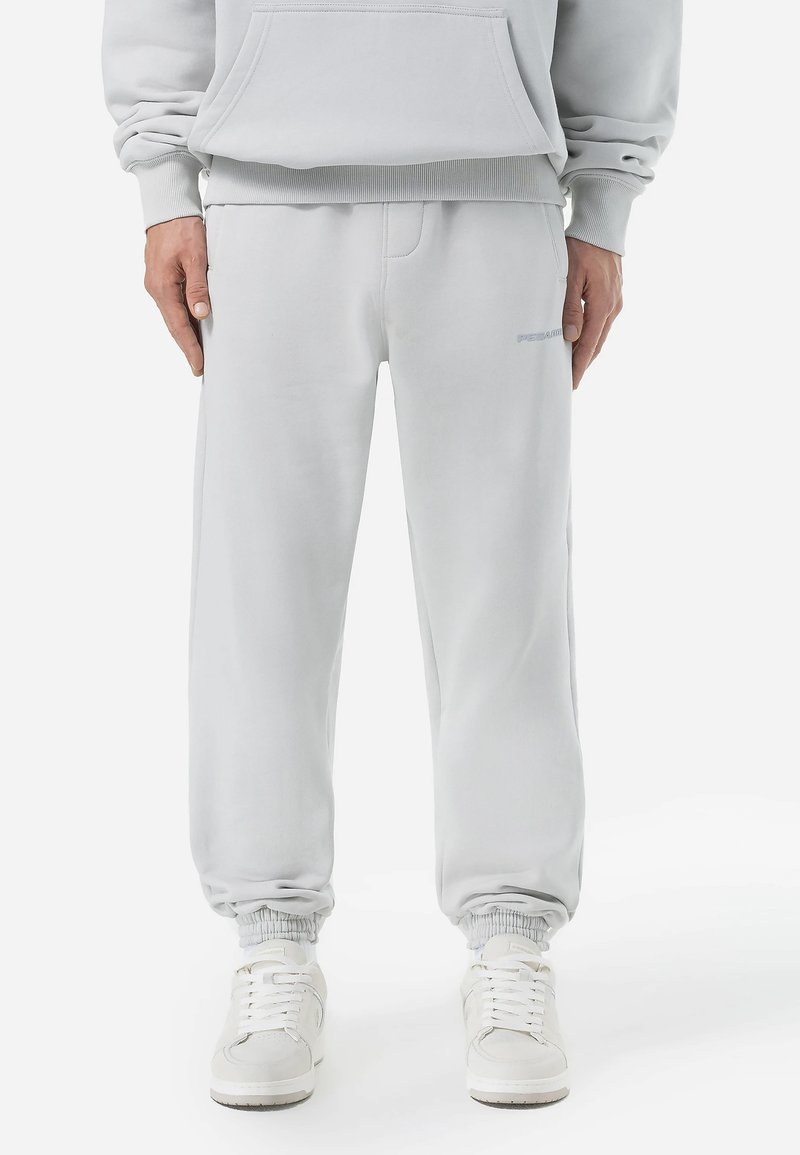 Pantalones de chándal de mezcla de algodón en gris claro con puños elásticos, cintura ajustable con cordón y un sutil detalle de logo en el lado izquierdo. Textura suave y corte relajado.