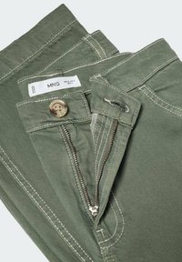 Pantalon en jean vert avec coutures blanches, fermeture éclair défaite, bouton fermé, et étiquette de marque MNG à l’intérieur de la ceinture.