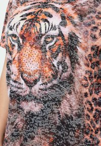 Krótki top z krótkim rękawem z grafiką tygrysa w kolorze pomarańczowym i czarnym z brokatowymi akcentami, na tle o fakturze i wielotonowym wzorze.