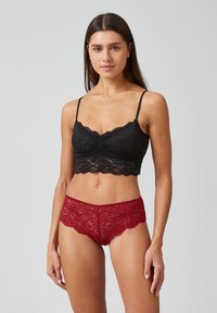 Zwarte kant bralette met dunne bandjes en geplooide details, gecombineerd met rode kant boyshorts met geschulpte randen en bloemmotieven.