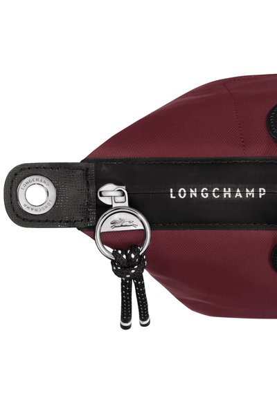Longchamp bag in burgundy nylon with black accents, featuring a silver ring, snap closure, and textured strap. Logo displayed prominently.