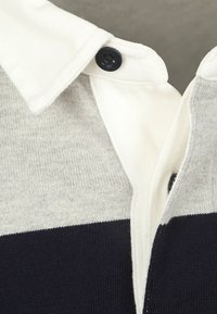 Polo shirt met een witte kraag, grijze bovenkant en marineblauwe onderkant. Gemaakt van zachte gebreide stof met knoopdetail bij de kraag.