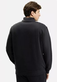 Czarny sweter z wysokim kołnierzem, z żebrowanymi mankietami i dołem. Wykonany z miękkiej tkaniny o gładkiej fakturze. Pokazany widok z tyłu.