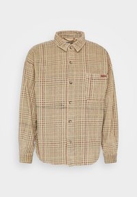Collared shirt in tan plaid fabric with red accents, front buttons, and left chest pocket. Textured, lightweight material.
