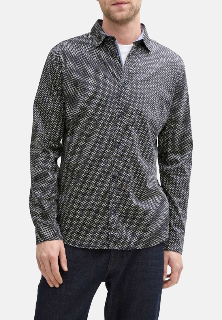 Chemise noire à manches longues avec un motif géométrique blanc, fermeture boutonnée à l'avant, et texture douce, associée à un jean foncé.